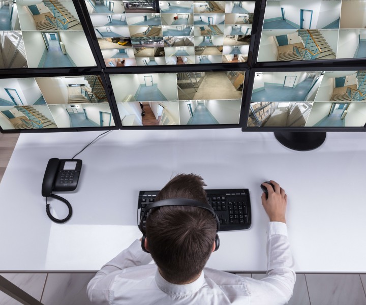 Elevated View Of Male Security Guard Monitoring Multiple Camera Footage On Computer At Workplace